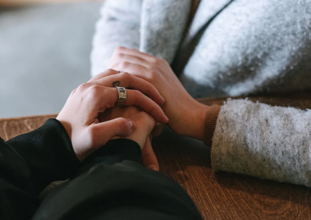 Two people holding hands in mutual support over a table.